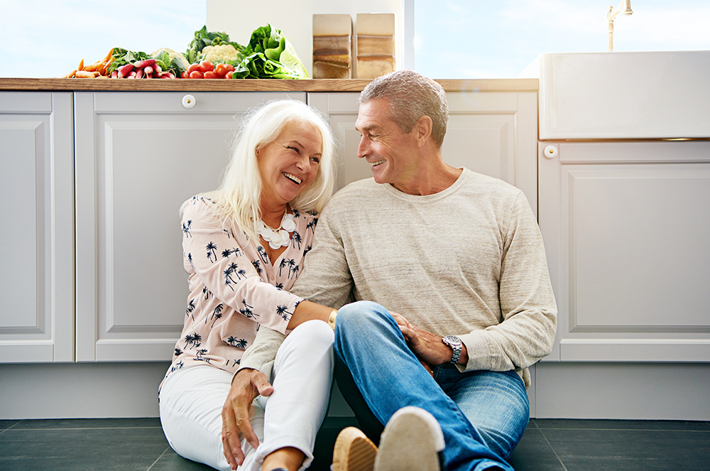 Mature couple sat on kitchen floor smiling at each other